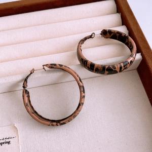 Détail de boucles d'oreilles créoles C à motif léopard sur un plateau à bijoux