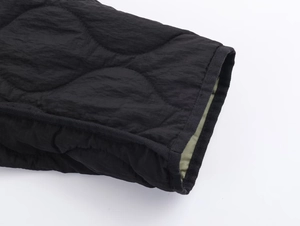 Close-up of black quilted jacket cuff with wave stitching and army green lining details