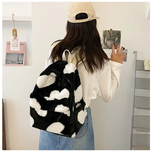 Detail of soft faux fur cow print backpack worn by model in a minimalist room