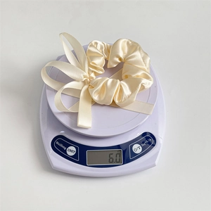 Detailed top view of a cream satin bow scrunchie on a scale weighing 6.0 grams
