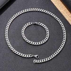 Detail of silver Cuban chain set featuring a matching necklace and bracelet on black background
