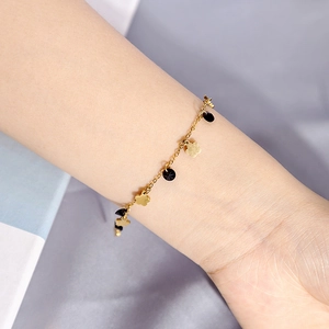 Detailed close-up of golden chain bracelet featuring black circular stones and floral charms