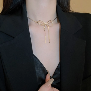 Detailed view of a gold bow tie pendant on a sleek snake chain worn by a model