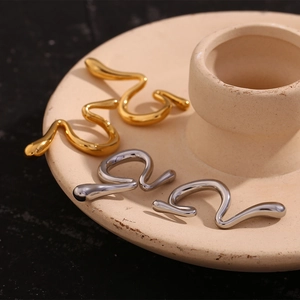 Close-up of wavy liquid metal ear cuffs in gold and silver finish on a beige plate