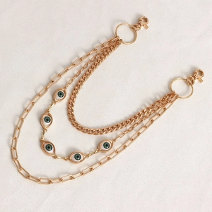 Detail of a layered gold-tone body chain featuring green evil eye charms and lobster clasps