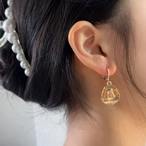 Detail of golden cowboy hat drop earring worn with a pearl hair clip on a model