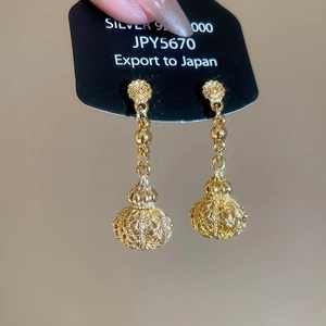 Detailed close-up of gold hollow lantern drop earrings with floral stud and silver pin
