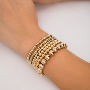 Close-up of layered golden beaded bracelets with heart charms on model's wrist