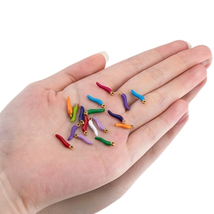 Miniature colorful chili pepper pendants in enamel finish held in hand to show scale