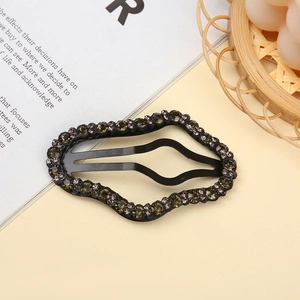 Detail of a wavy black metal hair clip decorated with dark grey rhinestones on beige background