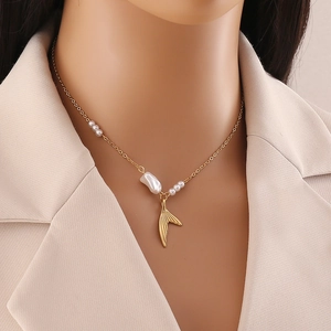 Golden mermaid tail necklace with irregular white pearls worn by a model in a beige blazer