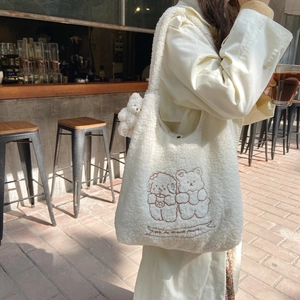 White plush tote bag with bear embroidery and charm shown on model in a cafe setting