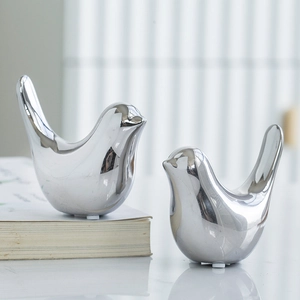 Macro shot of two silver bird ornaments with a smooth metallic finish and mirror reflection