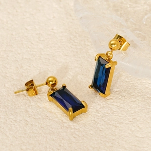 Golden geometric earrings with emerald-cut blue cubic zirconia on textured fabric