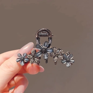 Detailed view of small grey flower hair claw clip with rhinestones held in hand