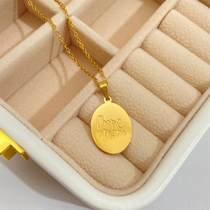 Macro detail of gold oval pendant featuring Carpe Diem engraving on a fine link chain