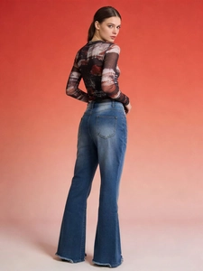 Rear view of blue flared jeans with frayed hems and a printed mesh long sleeve top