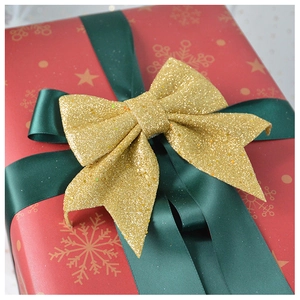 Close-up of golden glitter bow with dark green ribbon on red snowflake wrapping paper