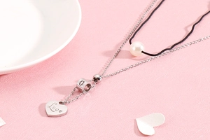 Detail of double-layer necklace with heart pendant and white pearl on pink background