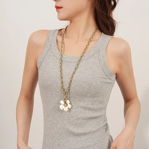 Detail of woven green and white cord necklace with textured gold flower pendant on model