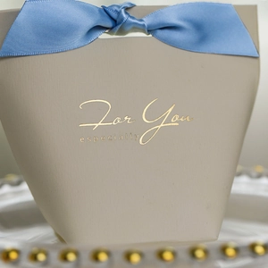Close-up of elegant beige wedding favor box with light blue ribbon and gold foil text