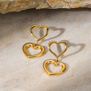 Close-up of double-layered gold heart pendant earrings on natural stone background