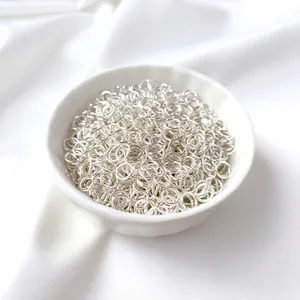 Shiny silver open jump rings in a ceramic bowl on white silk for DIY jewelry making