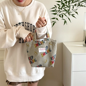 Close-up of beige corduroy tote bag with Keep Smiling print and metal button snap