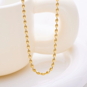 Close-up of a glossy gold oval bead chain necklace draped on a white ceramic cup