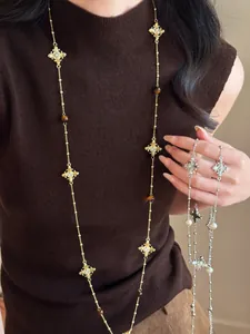 Détail de colliers vintage avec pendentif croix, perles œil de tigre et perles sur un pull