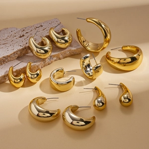 Minimalist gold geometric C-shaped and teardrop hoop earrings on a textured stone