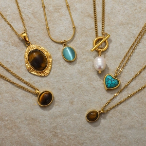 Detailed flat lay of golden stainless steel necklaces with tiger eye and pearl pendants