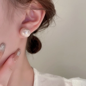 Detail view of large white pearl stud earring worn by model in minimalist French style