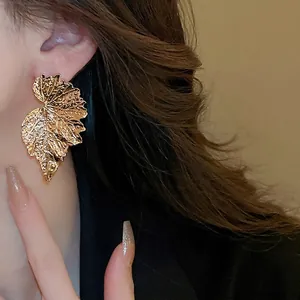 Golden oversized leaf-shaped metal earrings with textured finish on female model