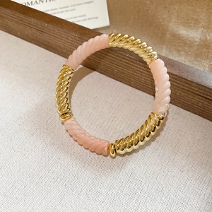Detail of pink and gold acrylic threaded beads on an elastic bracelet with warm lighting