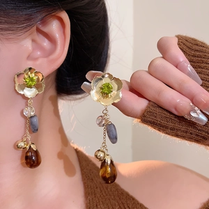Macro detail of long drop earrings featuring green stone flower and amber teardrop charm