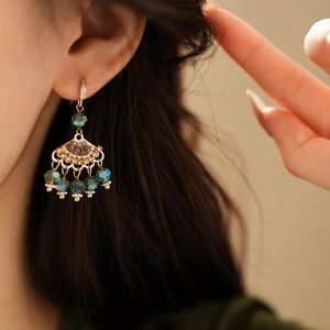 Detailed view of gold fan earring with zircon accents and teal beaded tassels on model
