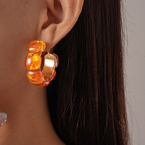 Close-up of amber resin C-shaped geometric hoop earrings on golden metal base worn by model