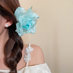 Détail d'une grande pince à cheveux en fleur de maille bleu clair sur les cheveux d'un mannequin.