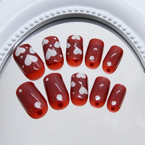 Glossy burgundy press-on nails with white heart and polka dot patterns on a mirror