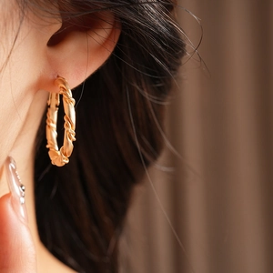 Close-up of golden twisted hoop earring in a minimalist style on a model ear