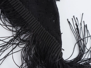 Macro shot of the black dress fabric showing tassel fringe edge and soft woven texture