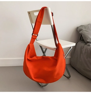 Detail of bright orange crescent bag made of Oxford cloth with wide adjustable shoulder strap