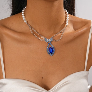 Detailed shot of bow-knot pearl necklace with blue teardrop gemstone on model