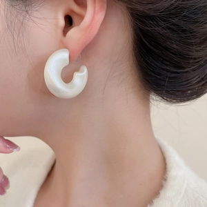 Detail of white pearlescent C-shaped acrylic earrings on model for a minimalist style