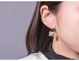 Close-up of a silver windmill drop earring worn by a model in a natural setting