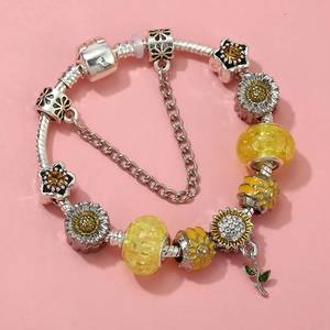 Macro detail of silver snake chain bracelet with yellow sunflower enamel charms