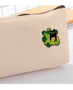 Close-up of a black cat on a yellow gift box enamel pin on a beige canvas bag