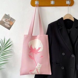 Detail of pink knitted tote bag featuring a white cat and flower pattern on a wall hook