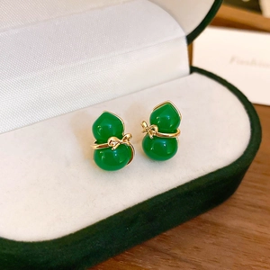 Macro detail of green translucent gourd earring with a gold bow in a velvet jewelry box